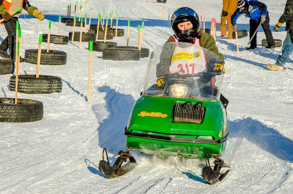 Tracey Porreca is seated on a bright green snowmobile surrounded by snow and tires set up as a boundary.