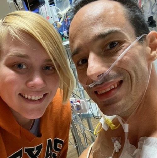 Male presenting heart and kidney transplant recipient Lukas has light tan skin, dark eyes, and short dark hair. He is smiling in a hospital setting with an oxygen tube over his face. To his right is a female presenting person with angle cut blonde hair and a big smile.