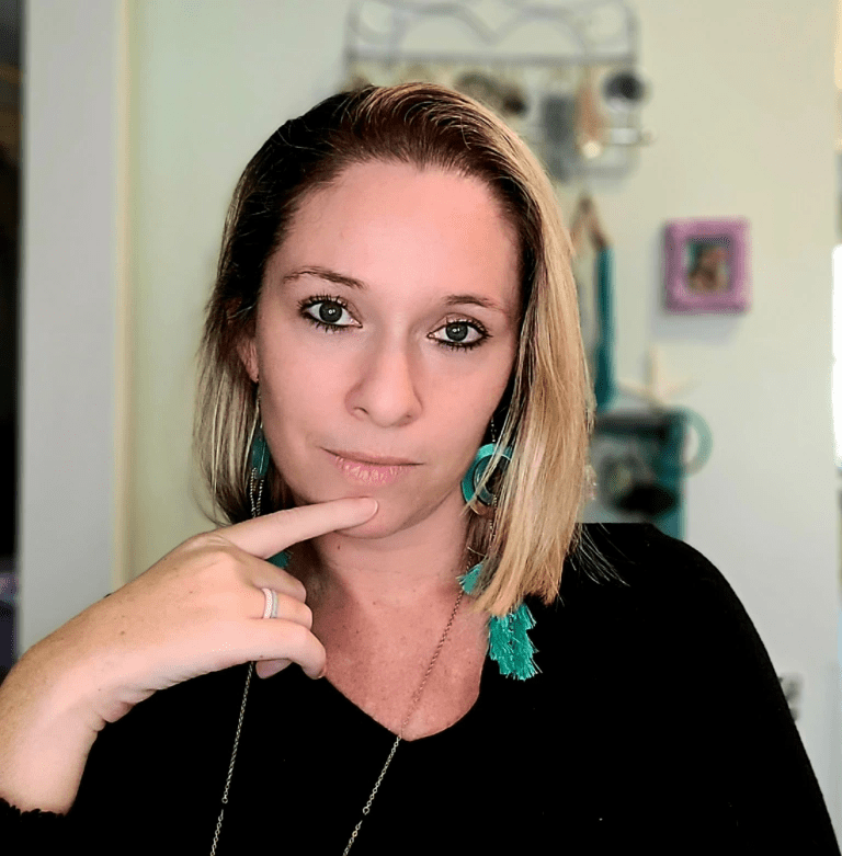 This portrait shows Ali Ingersoll with short-cropped blonde hair, brown eyes, and white skin wearing a black scoop shirt and gaudy green earrings.