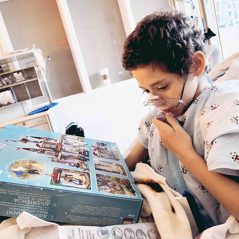 12-year-old Viktoria is pictured with short brown hair in a hospital bed with a respirator mask over her face as she looks at a toy.
