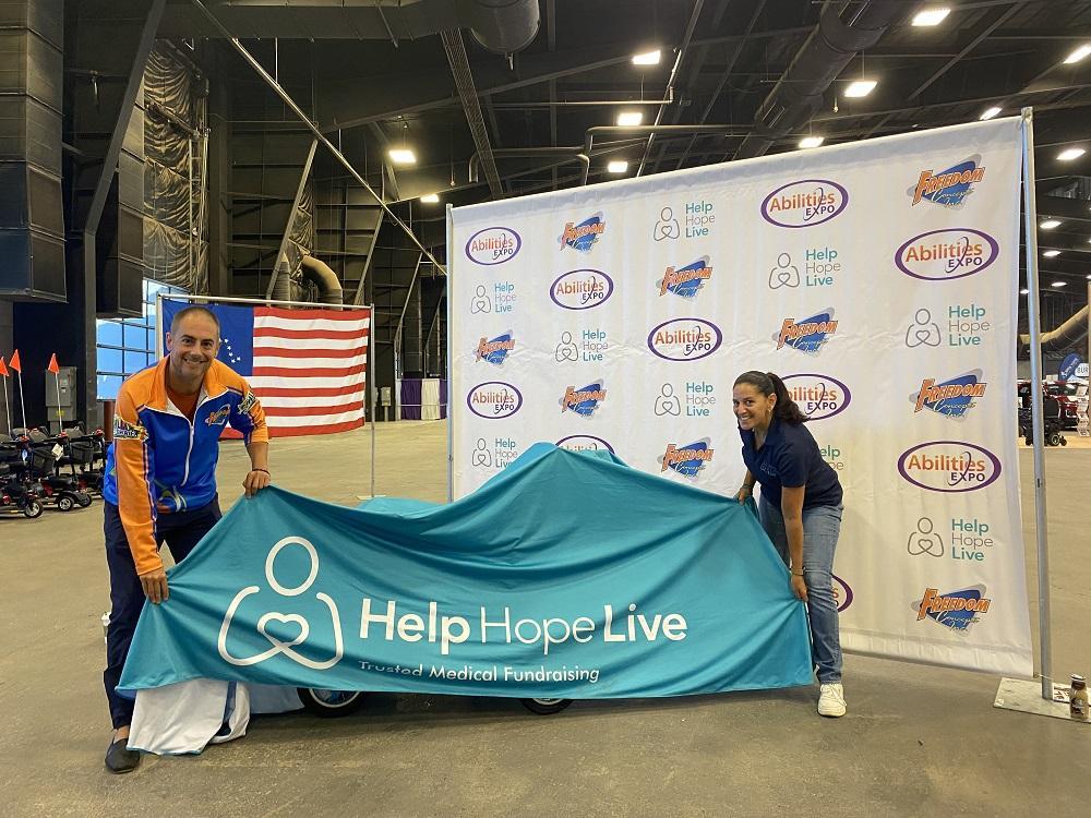 James Wall from Freedom Concepts and Kelly L Green from Help Hope Live hold either side of a teal cover over the new adaptive bike we’re giving to 3-year-old Emberly. They are at the Abilities Expo Phoenix.