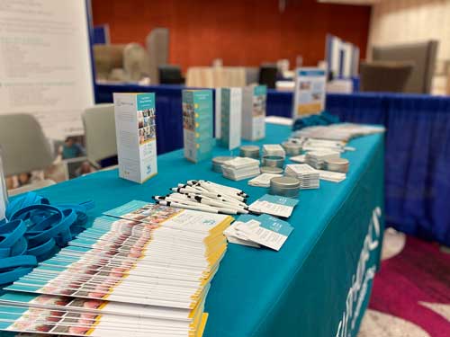 Exhibition table displaying brochures, flyers, pens, and promotional materials
